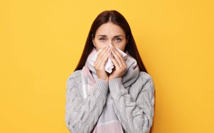femeie răcită, cu imunitate slăbită, care își suflă nasul