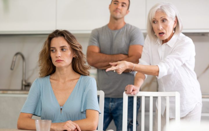 soacra o ceartă pe noră în bucătărie, iar fiul stă cu brațele încrucișate