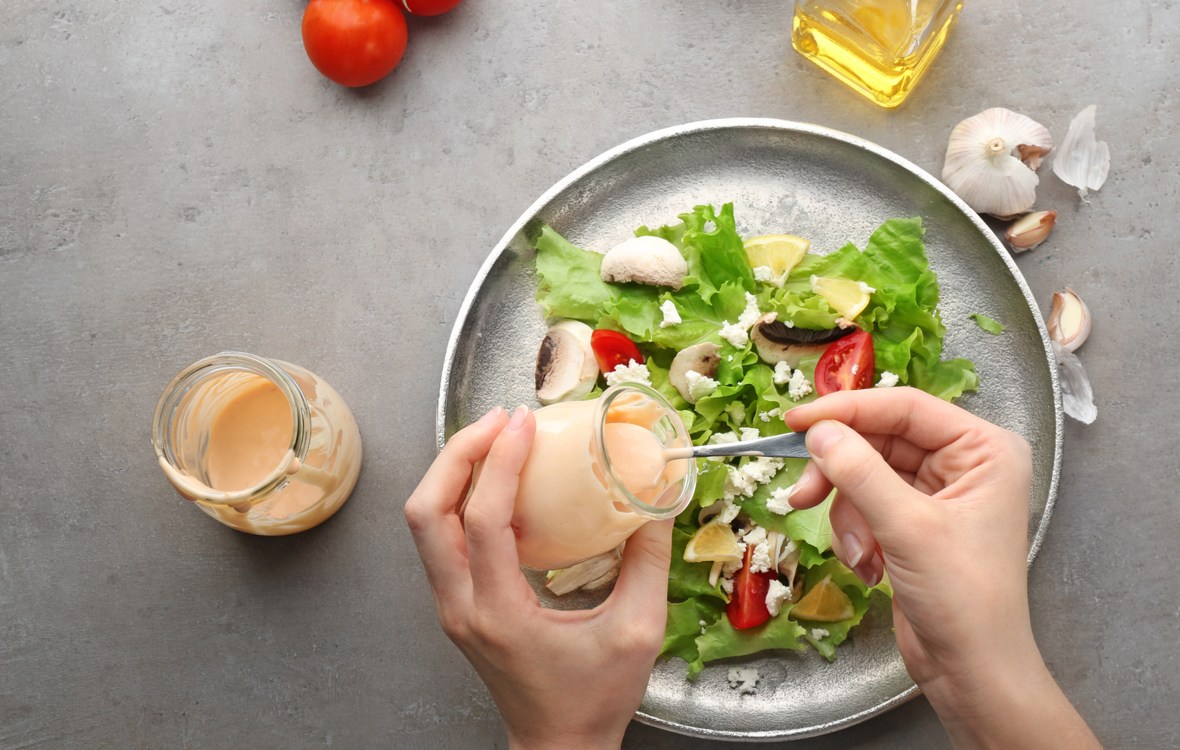 dressing salata cele mai sanatoase optiuni. salata verde cu rosii si putina branza peste care o femeie toarna dressing cu lingurita
