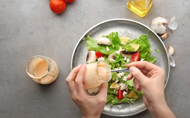 dressing salata cele mai sanatoase optiuni. salata verde cu rosii si putina branza peste care o femeie toarna dressing cu lingurita