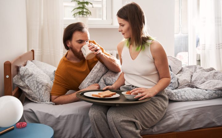 femeie care îi aduce micul dejun la pat partenerului ei