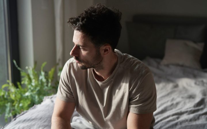 bărbat trist, în pat, cu probleme de somn din cauza deficitului de serotonină