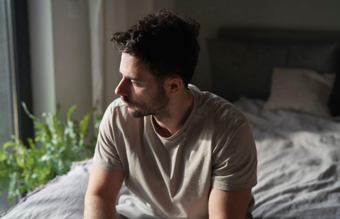 bărbat trist, în pat, cu probleme de somn din cauza deficitului de serotonină