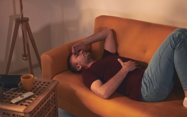 bărbat cu inflamație în corp, bolnav, stă întins pe canapea