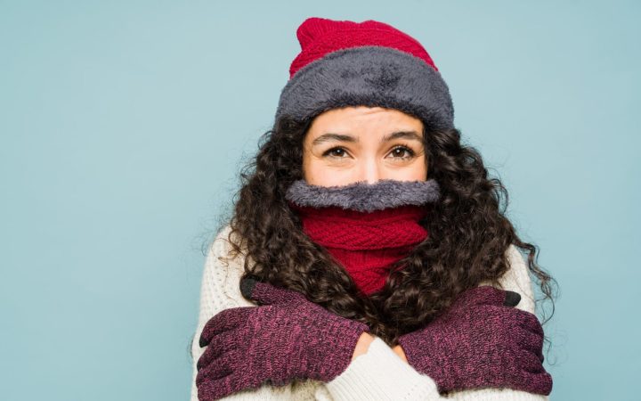 femeie cu tiroidita hashimoto foarte friguroasă, cu căciulă, fular tras pe nas și mănuși la interior