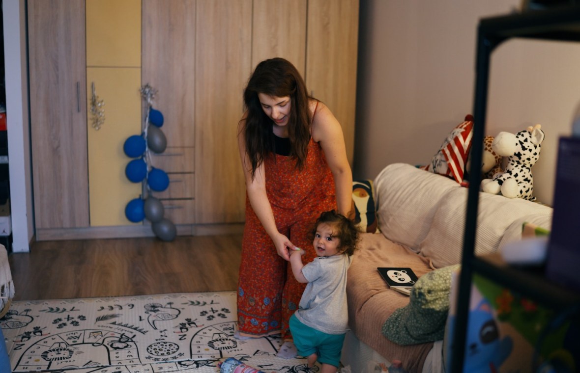 mama, sandra, își susține fiul de 1 an, Anton care învață să meargă în sufragerie