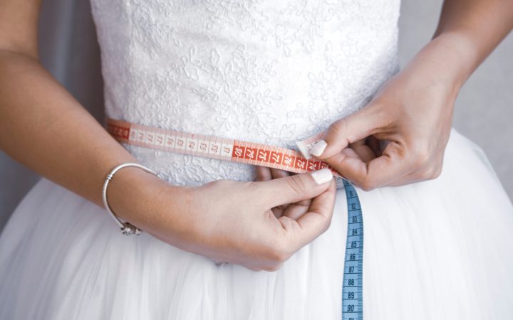 femeie în rochie de mireasă cu corset își măsoară talia