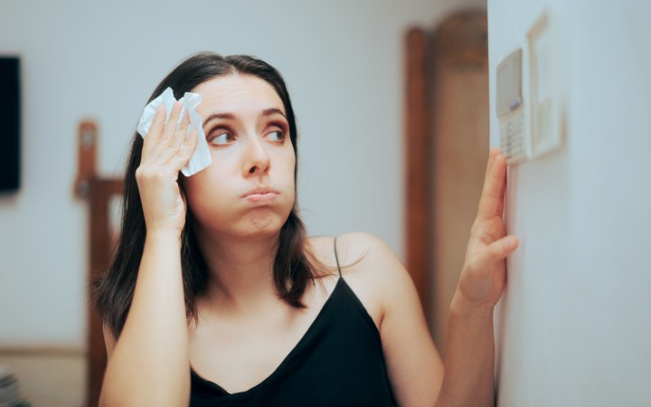 Femeie încălzită își șterge transpirația și setează temperatura aerului condiționat