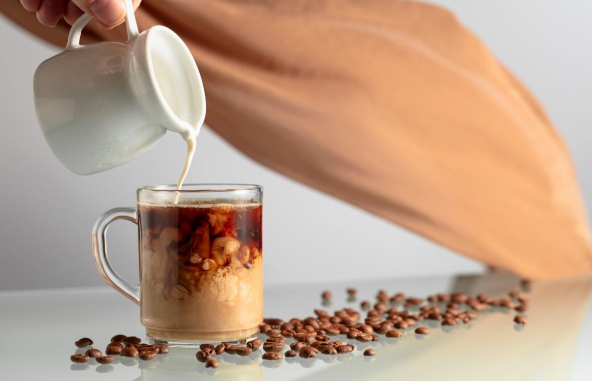 ceașcă transparentă de cafea în care se toarnă lapte