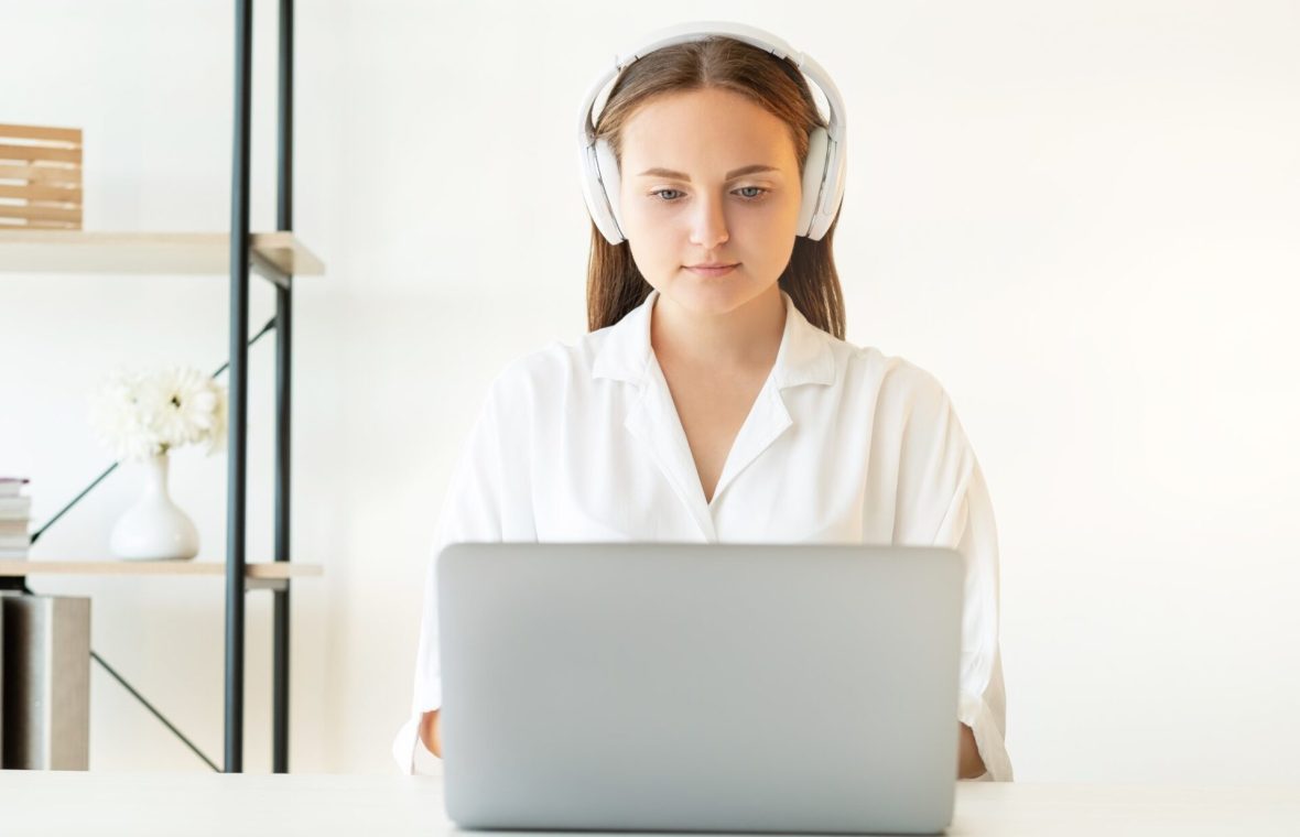 femeie care ascultă sunete albe în căști în timp ce muncește la laptop