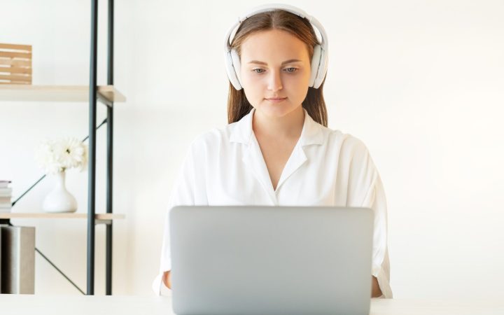 femeie care ascultă sunete albe în căști în timp ce muncește la laptop