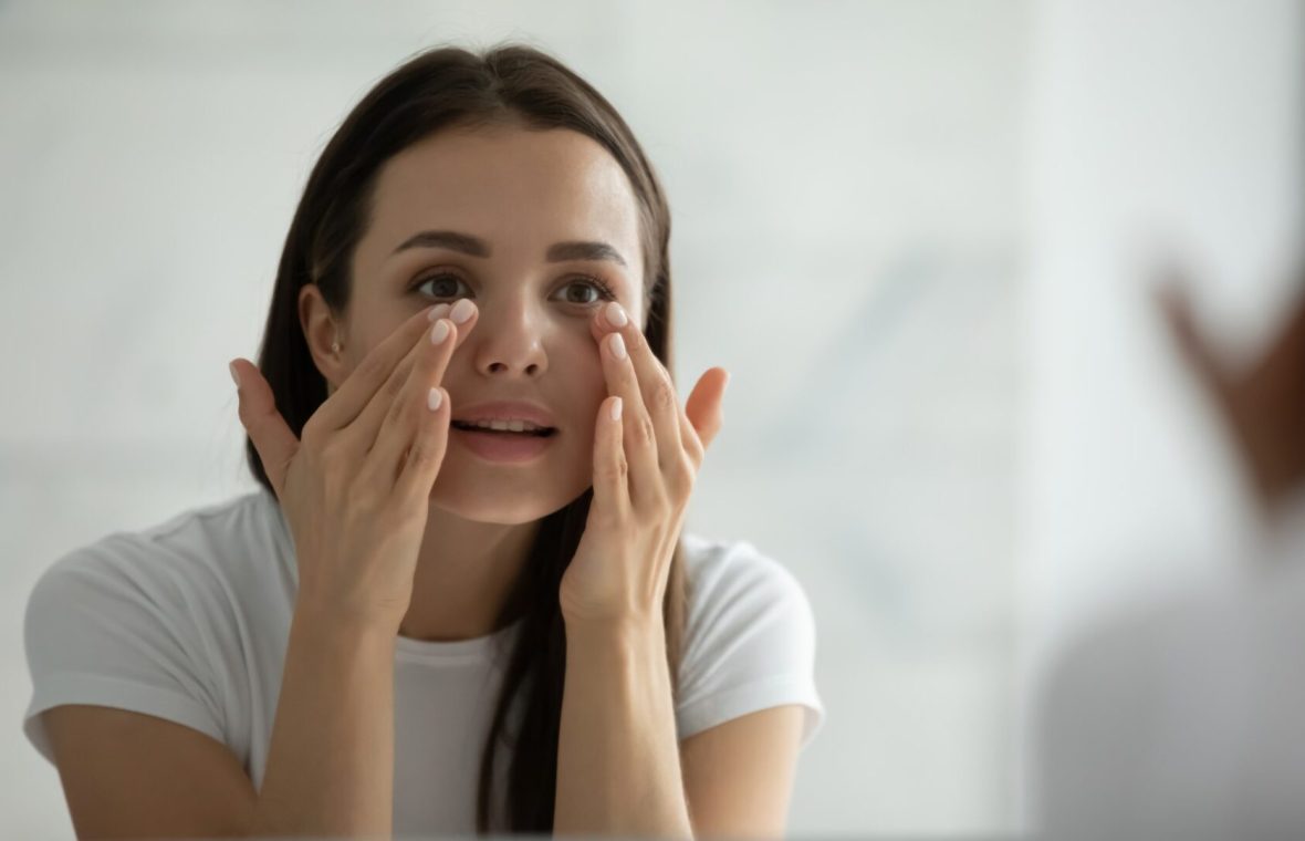 femeie tânără face masaj facial în oglindă