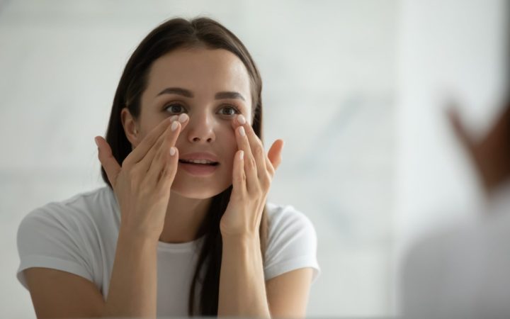 femeie tânără face masaj facial în oglindă