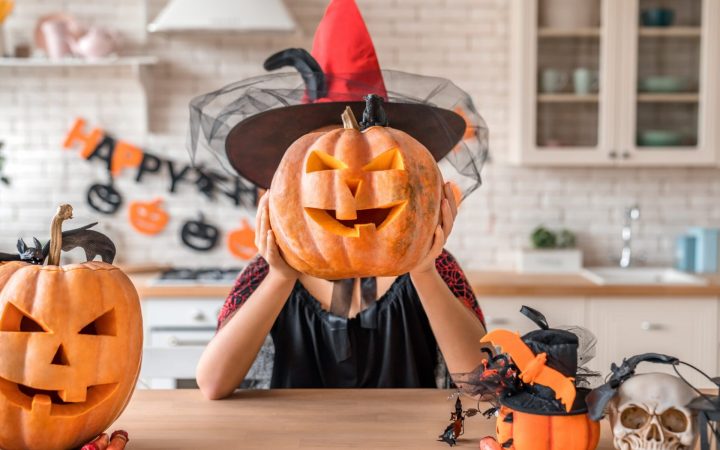 dovleci de halloween sculptați, femeie costumată în vrăjitoare ține un dovleac sculptat în dreptul capului