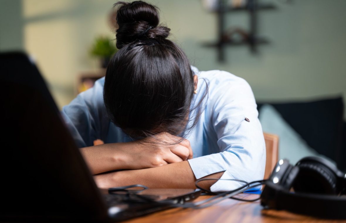 sănătatea mintală la muncă - femeie cu capul pe birou în burnout la job