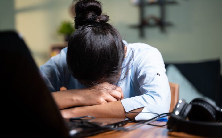 sănătatea mintală la muncă - femeie cu capul pe birou în burnout la job