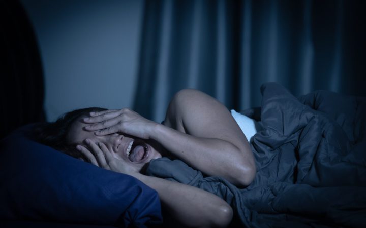 femeie care visează urât și e trezită din somn de un coșmar