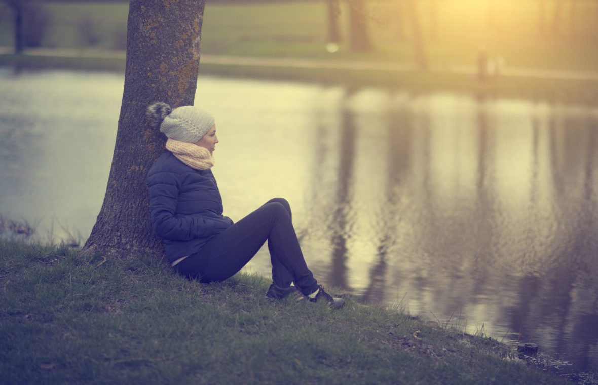 femeie singură contemplativă, toamna târziu, la apus, pe malul lacului, în parc
