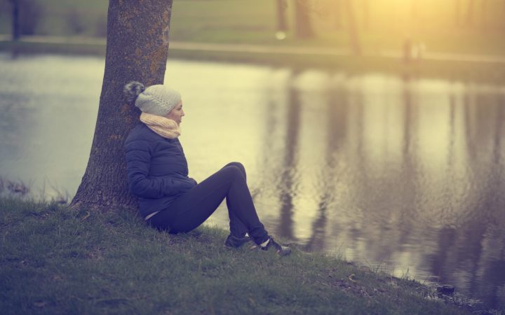 femeie singură contemplativă, toamna târziu, la apus, pe malul lacului, în parc
