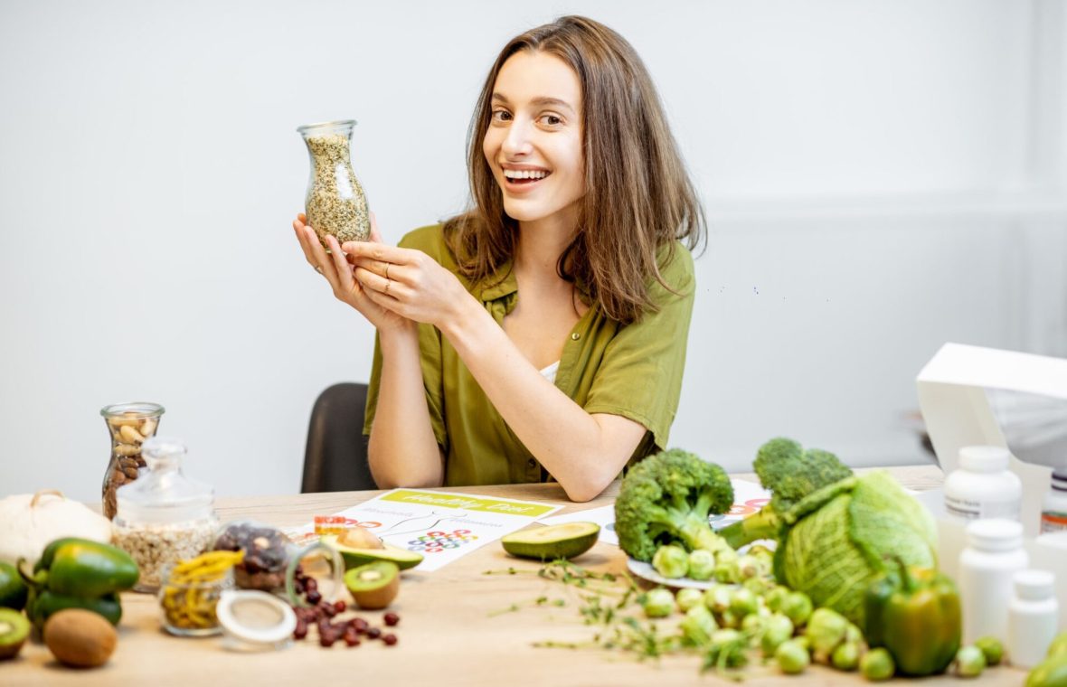 femeie slabă și fericită cu un borcan cu cereale în mână și broccoli și alte alimente din dieta oshawa macrobiotică pe masă