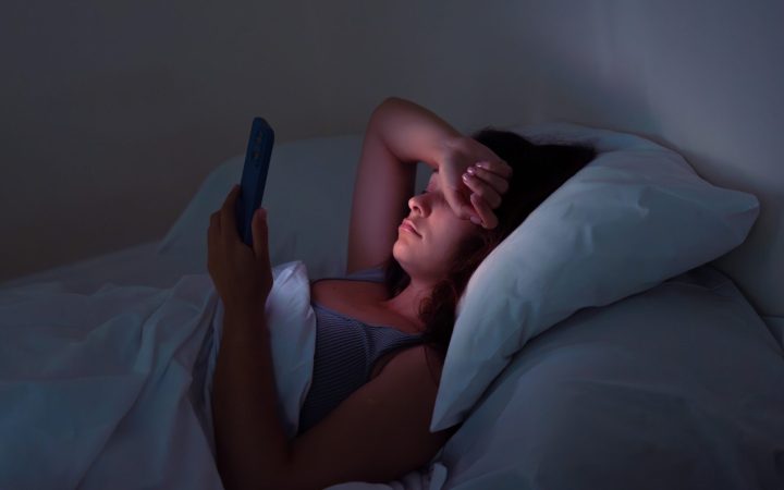 Femeie care scrollează pe telefon noaptea, în pat în loc să doarmă, are insomnie