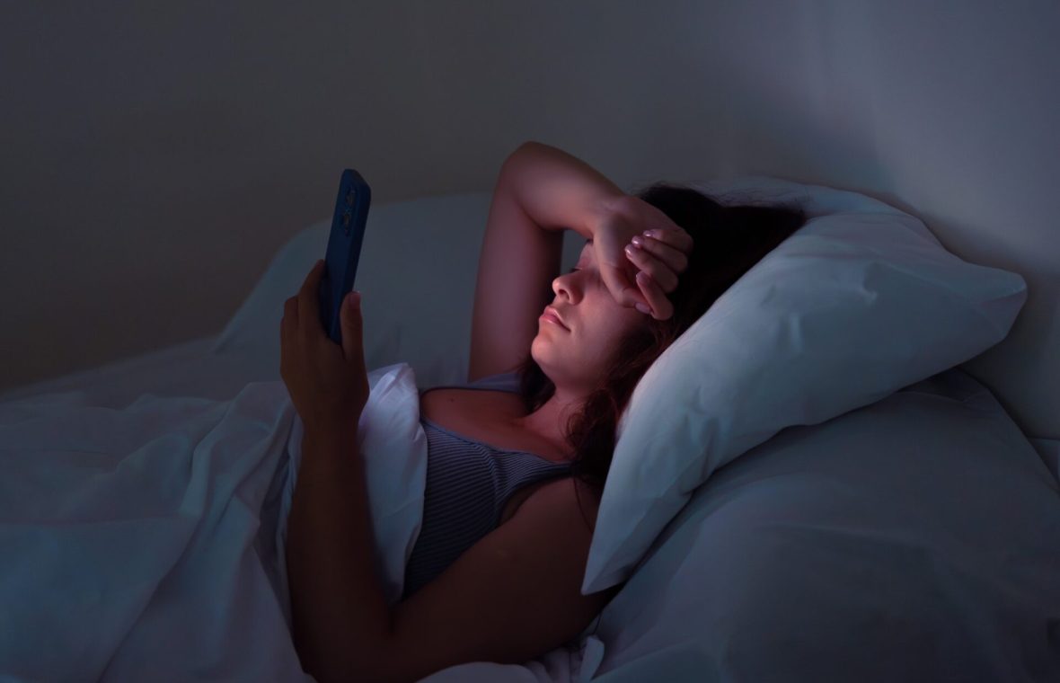 Femeie care scrollează pe telefon noaptea, în pat în loc să doarmă, are insomnie