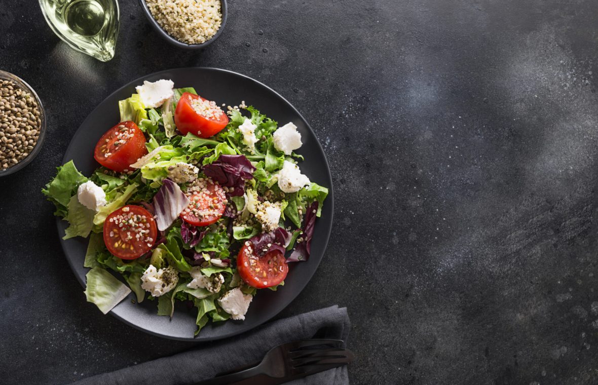 salată verde, radicchio, roșii, mozarella și semințe de cânepă decorticate, alături de o lingură cu semințe de cânepă și ulei