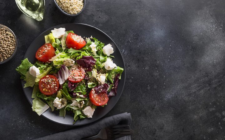 salată verde, radicchio, roșii, mozarella și semințe de cânepă decorticate, alături de o lingură cu semințe de cânepă și ulei