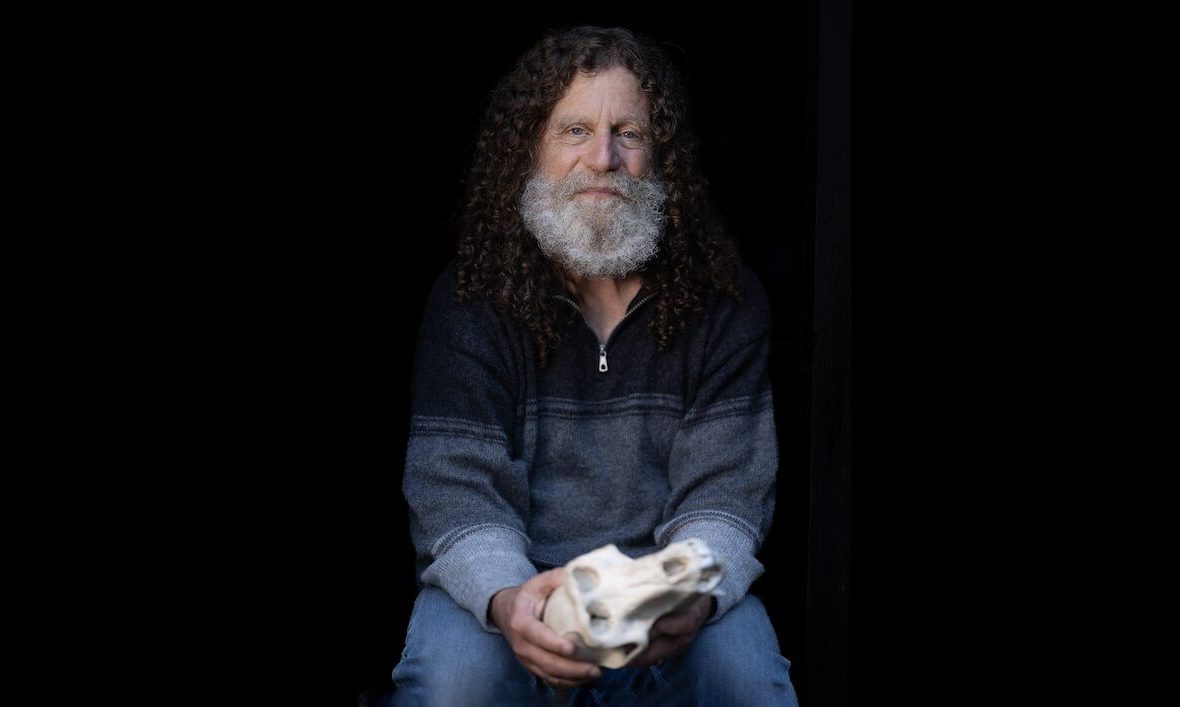 Robert Sapolsky, profesor în neuroștiințe la Stanford, stă pe un un scaun, într-un decor negru, cu un craniu în mână