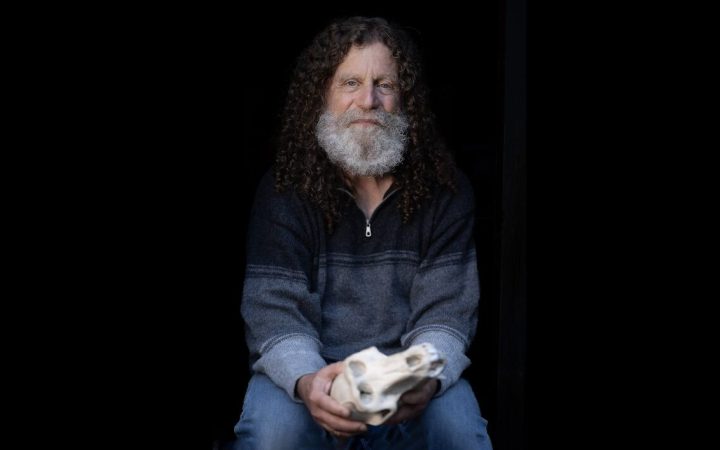 Robert Sapolsky, profesor în neuroștiințe la Stanford, stă pe un un scaun, într-un decor negru, cu un craniu în mână