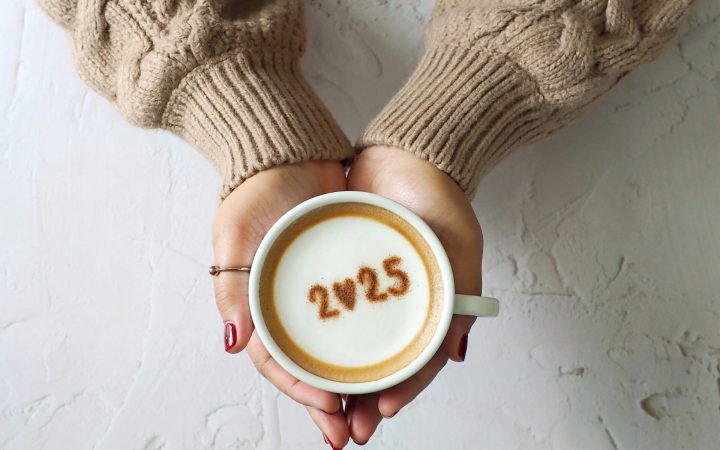 femeie cu pulover mocha mousse și cu o cafea cu spumă de lapte în mână, cu cafea e scris 2025