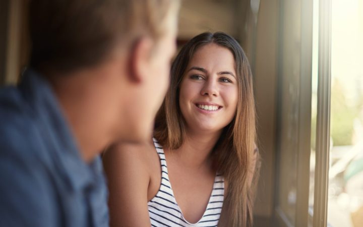 Un cuplu în care bărbatul e cu spatele, iar femeia extrovertită zâmbește