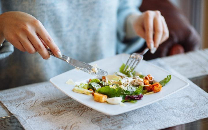 femeie plinuță mănâncă salată caesar cu dressing și multe calorii