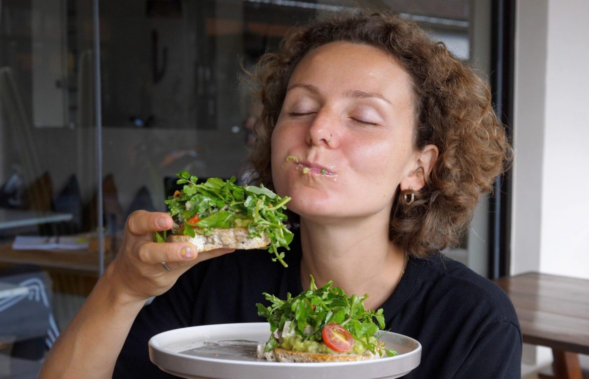 femeie care mănâncă cu poftă dintr-o felie mică de pâine cu o cantitate mare de salată și avocado - dieta volumetrică - și se murdărește la gură