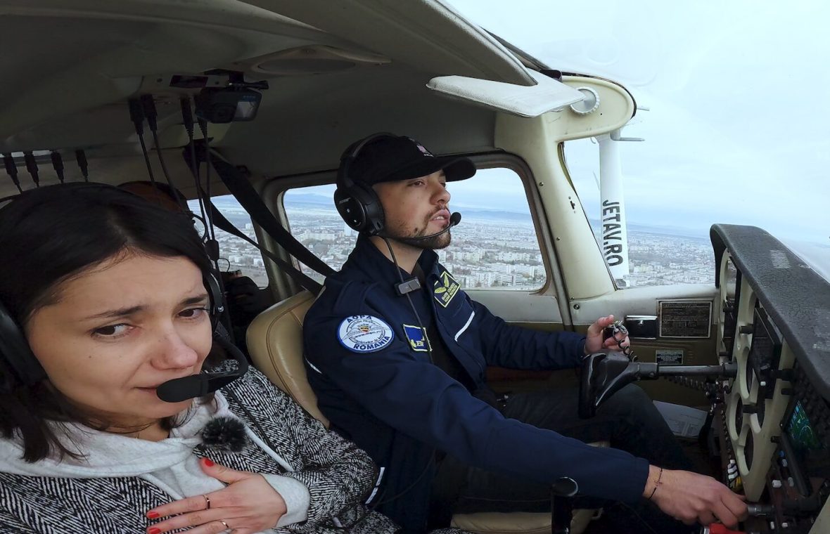 Reporter SmartLiving în timp ce învață să piloteze un avion de dimensiuni mici cu ajutorul pilotului Mihai Stănescu. Reporterul este speriată, își ține mâna la inimă