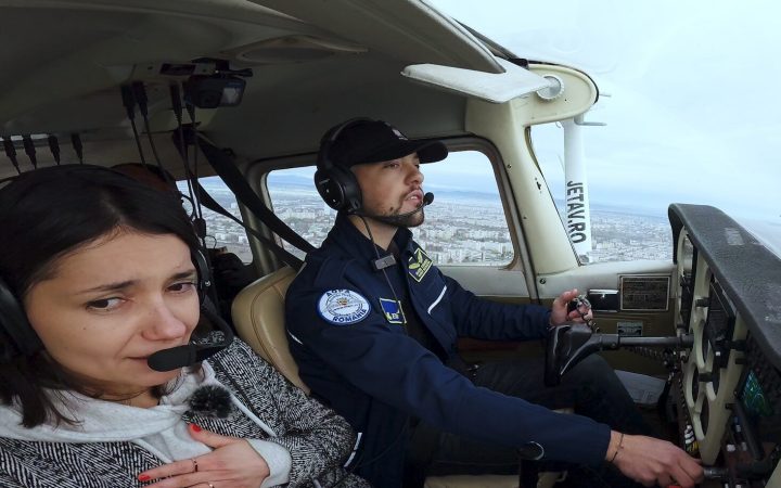 Reporter SmartLiving în timp ce învață să piloteze un avion de dimensiuni mici cu ajutorul pilotului Mihai Stănescu. Reporterul este speriată, își ține mâna la inimă