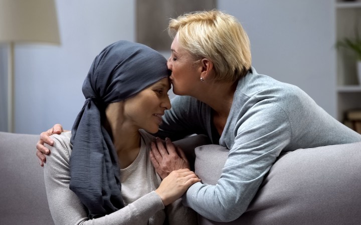 pe o canapea stau o mamă și o fiică, mama își sărută fiica diagnosticată cu cancer a sân sprijin emoțional