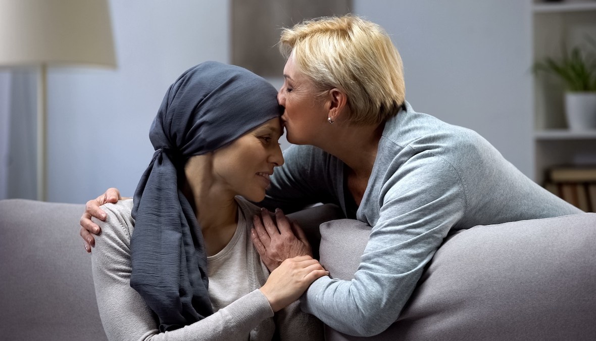 pe o canapea stau o mamă și o fiică, mama își sărută fiica diagnosticată cu cancer a sân sprijin emoțional