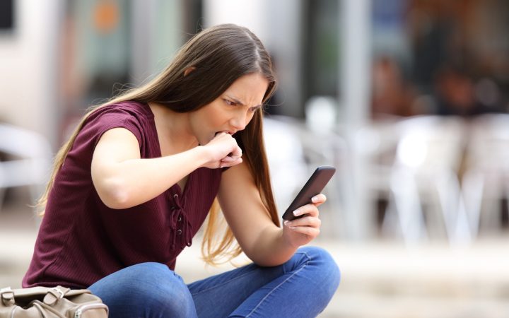 adolescentă cu telefonul în mână furioasă își mușcă pumnul