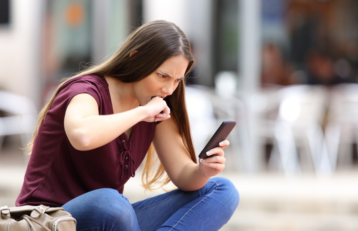 adolescentă cu telefonul în mână furioasă își mușcă pumnul