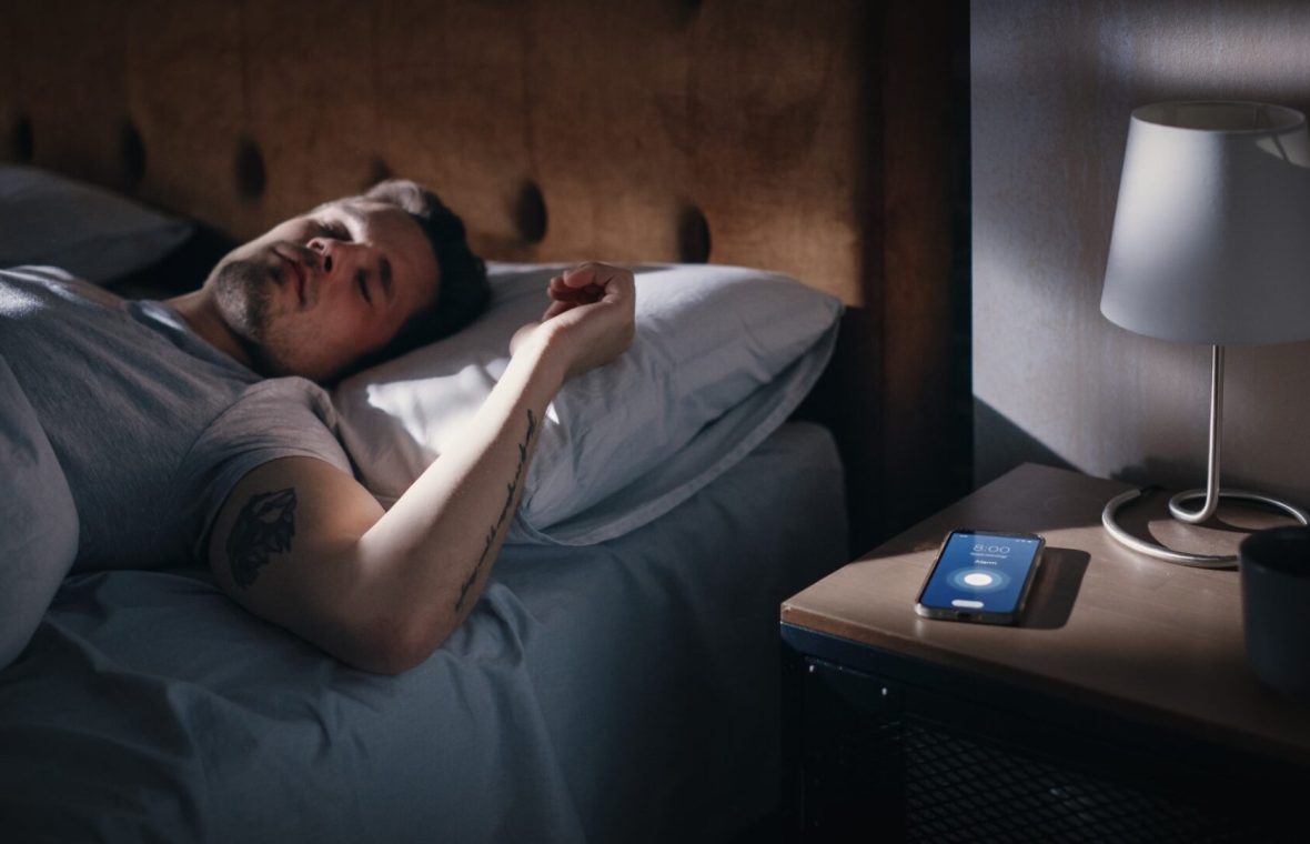 bărbat care doarme și nu e trezit de alarma telefonului - ce se întâmplă când dormi prea mult