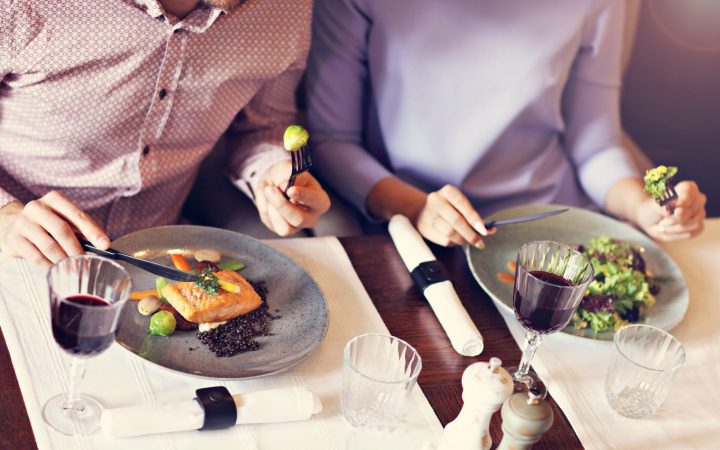 cuplu la cină care mănâncă somon și legume verzi pentru a scădea nivelul de prolactină