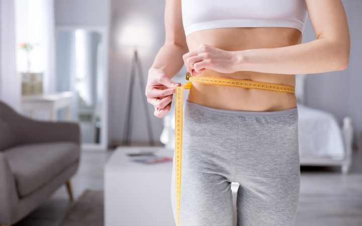 cum să te îngrași: femeie foarte slabă care își măsoară talia cu un centimetru