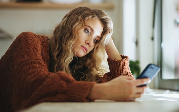 femeie tânără tristă se uită pe telefon în casa ei singură