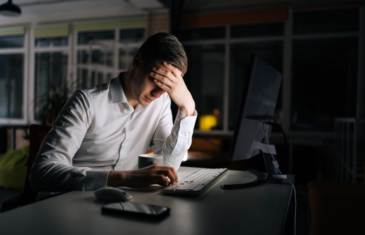 bărbat cu multe ore de muncă peste program, obosit, noaptea la birou