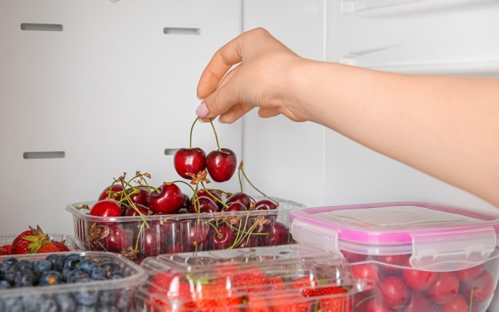 femeie ia cireșe dintr-o caserolă de plastic din frigider