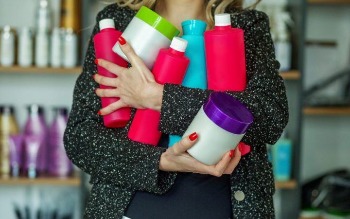 femeie ține în brațe multe creme și loțiuni pentru piele
