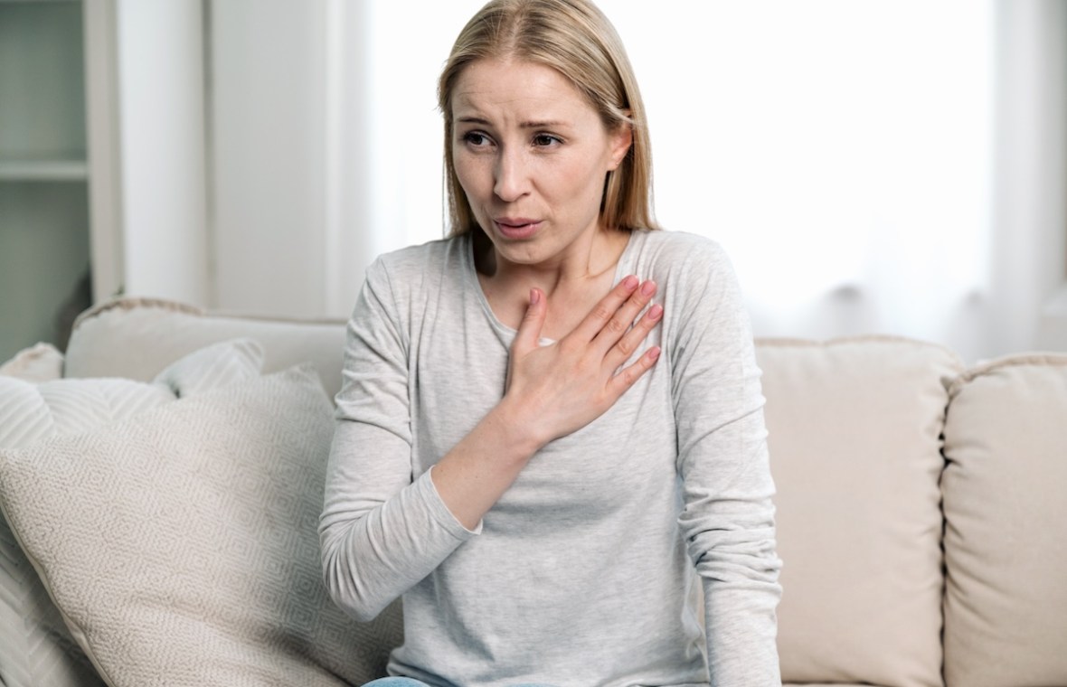 femeie stă pe canapea atac de panică frică ține mâna la piept respiră profund