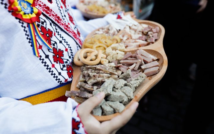 Femeie în haine tradiționale cu un platou cu specialități din carne tradiționale românești