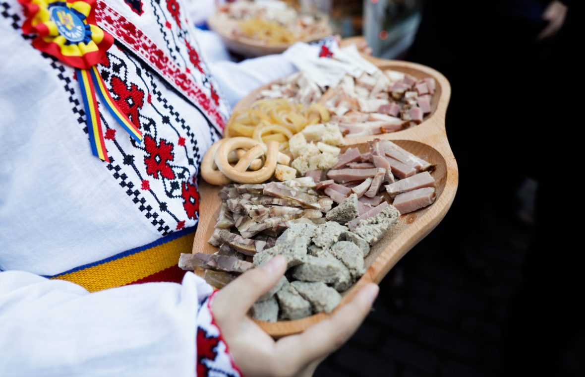 Femeie în haine tradiționale cu un platou cu specialități din carne tradiționale românești